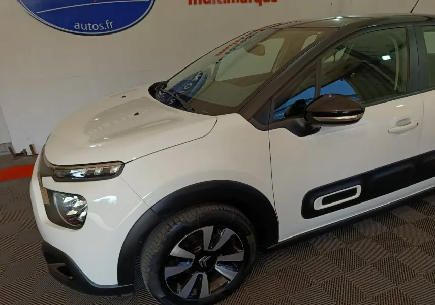 Vue 3/4 avant droit d'une Citroën C3 blanche avec protections latérales noires et jantes bicolores.
