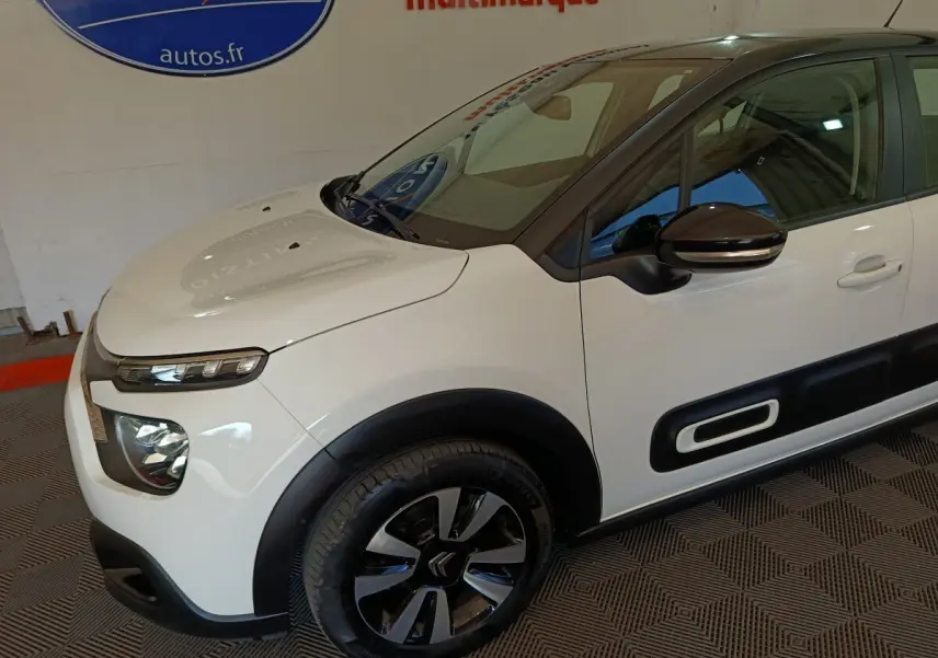 Vue 3/4 avant droit d'une Citroën C3 blanche avec protections latérales noires et jantes bicolores.