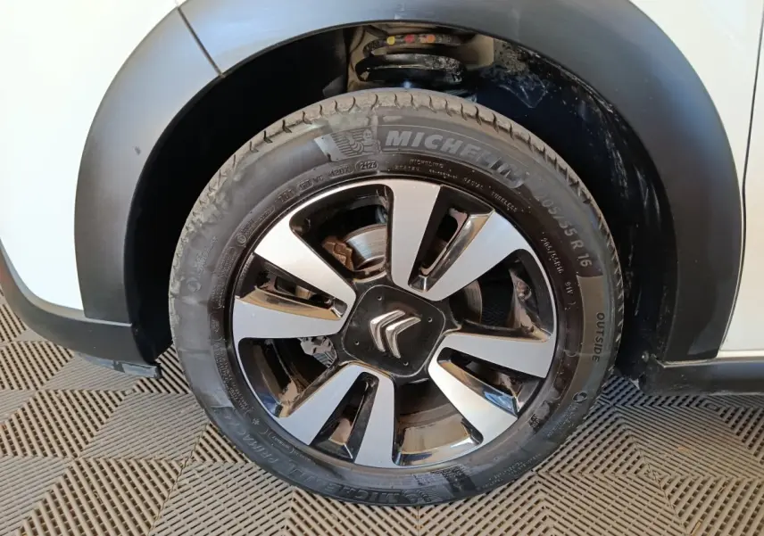 Gros plan sur la roue avant gauche d'une Citroën C3 blanche, jante alliage bicolore avec logo Citroën central.