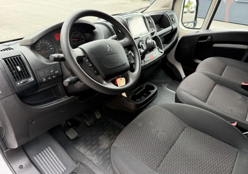 Vue intérieure côté conducteur du Peugeot Boxer Fourgon 2023, volant multifonctions et sièges tissu gris à motifs rouges.