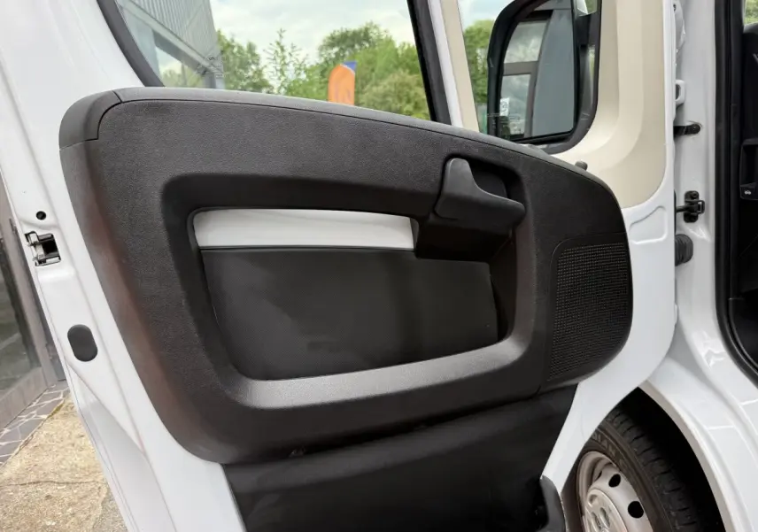 Vue rapprochée de la porte avant gauche blanche du Peugeot Boxer Fourgon 2023 avec poignée noire et haut-parleur intégré.