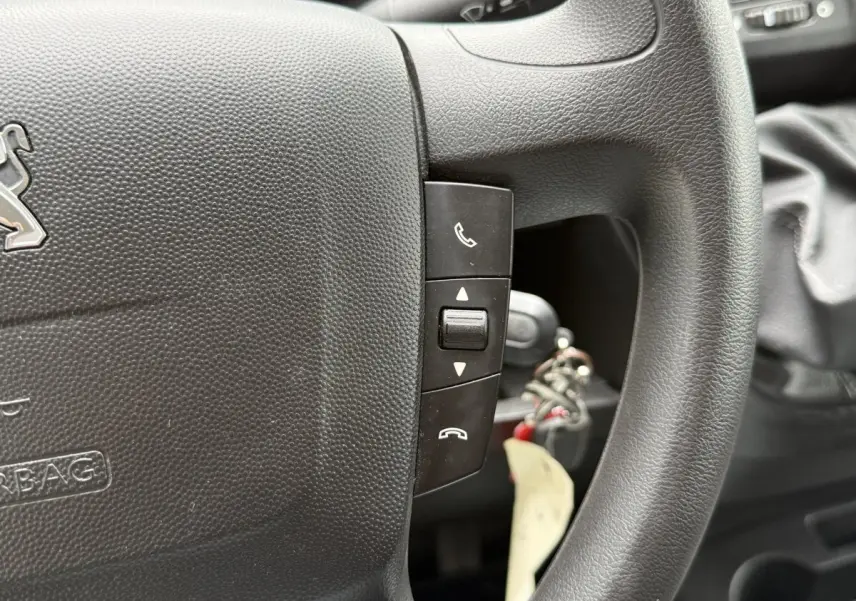 Gros plan sur le volant multifonctions noir du Peugeot Boxer Fourgon 2023 avec commandes d’appel et clé insérée.