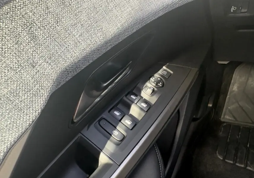 Gros plan sur la commande des vitres côté gauche de la Peugeot 3008 Hybrid noire, avec habillage tissu gris et plastique noir.