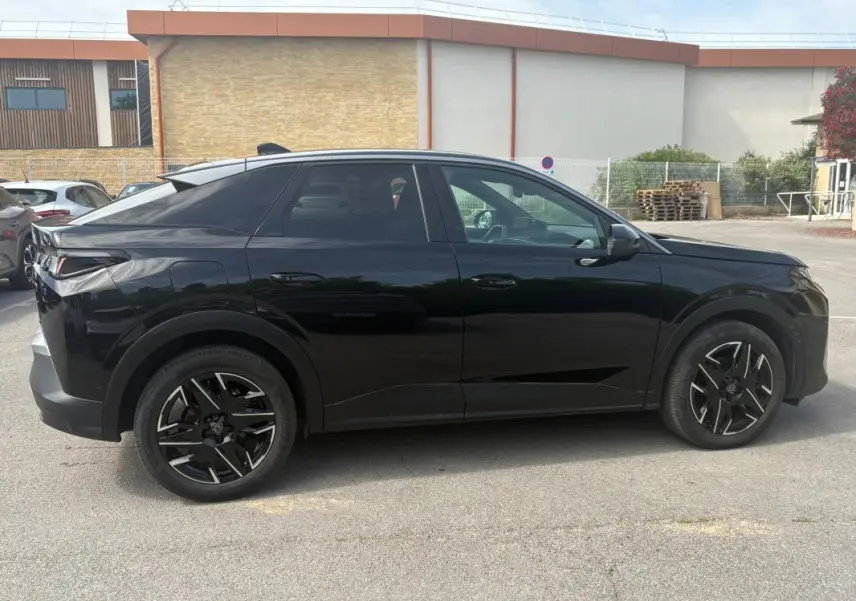 Profil côté gauche du Peugeot 3008 Hybrid noir de 2025 avec jantes alliage noires de 19 pouces, en extérieur sur parking.
