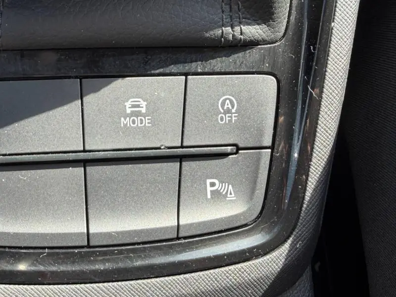 Gros plan sur les boutons de commande du mode conduite et assistance au stationnement dans une Skoda Scala noir Magic nacré.