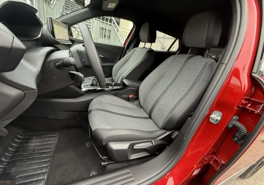 Vue intérieure côté conducteur du Peugeot 2008 rouge elixir 2025, sièges tissu gris et console centrale avec boîte manuelle.