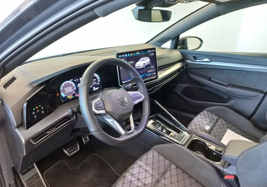 Vue intérieure côté conducteur de la Volkswagen Golf 1.5 eTSI R-Line 2025 avec écran tactile et sellerie tissu gris à motif.