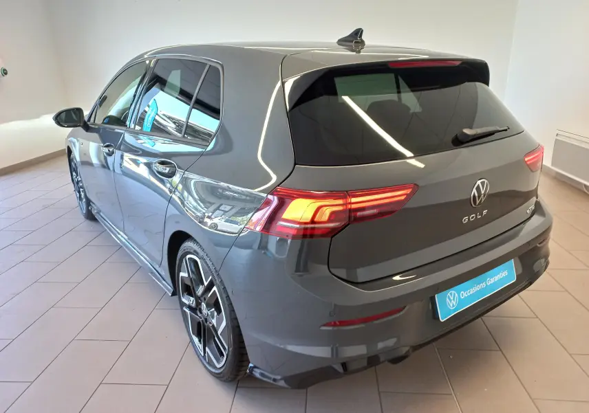 Volkswagen Golf 1.5 eTSI R-Line gris dauphin vue 3/4 arrière droit avec feux allumés en intérieur showroom.