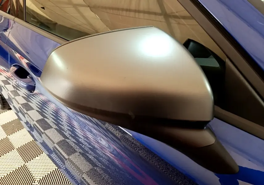 Rétroviseur côté gauche argenté sur SEAT Leon bleu, vue rapprochée du côté conducteur avec reflet au sol.