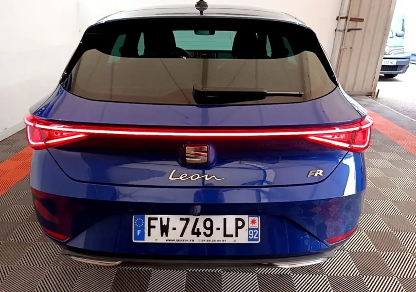 Vue arrière d'une SEAT Leon FR bleu avec feux arrière LED en bandeau lumineux allumé dans un garage.