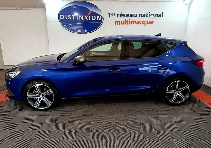 Vue de profil côté gauche d'une SEAT Leon bleu 2021 avec jantes alliage et rétroviseurs argentés dans un showroom.