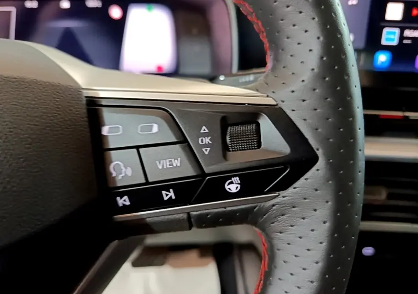 Gros plan sur les commandes gauche du volant en cuir noir perforé avec surpiqûres rouges du SEAT Leon bleu 2021.