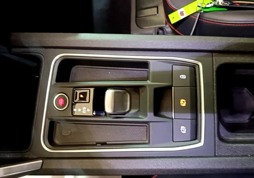 Vue rapprochée de la console centrale noire du SEAT Leon 1.5 eTSI avec levier de vitesse automatique et boutons de frein à main.
