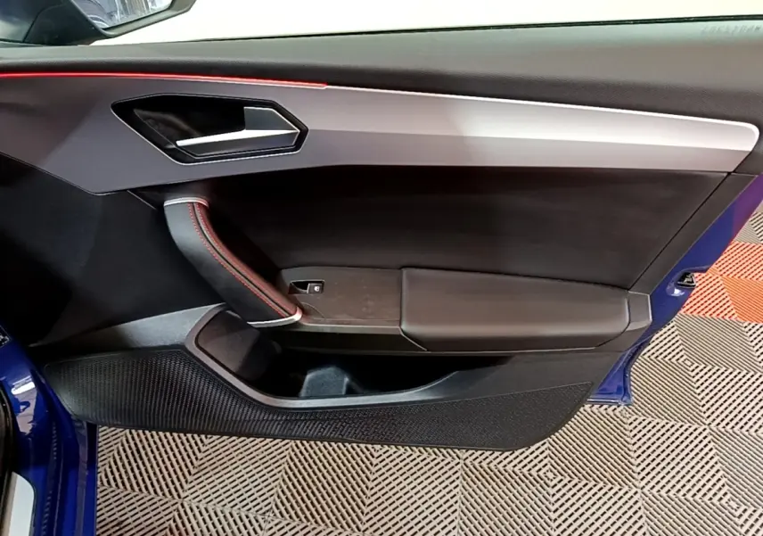 Vue intérieure côté gauche de la porte avant bleu avec surpiqûres rouges et poignée intégrée du SEAT LEON 1.5 eTSI 2021.