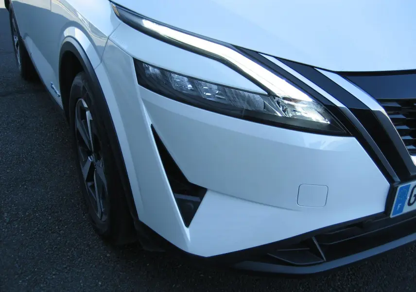 Vue 3/4 avant droit du Nissan Qashqai blanc nacré, mettant en valeur son phare LED et la calandre noire distinctive.