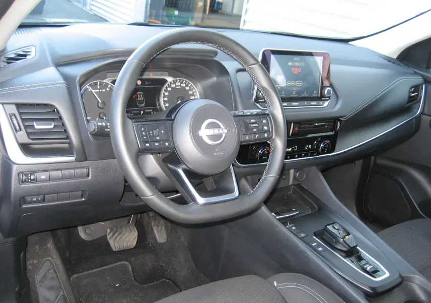 Vue intérieure côté conducteur du Nissan Qashqai 2024, tableau de bord noir avec écran tactile et volant multifonction.