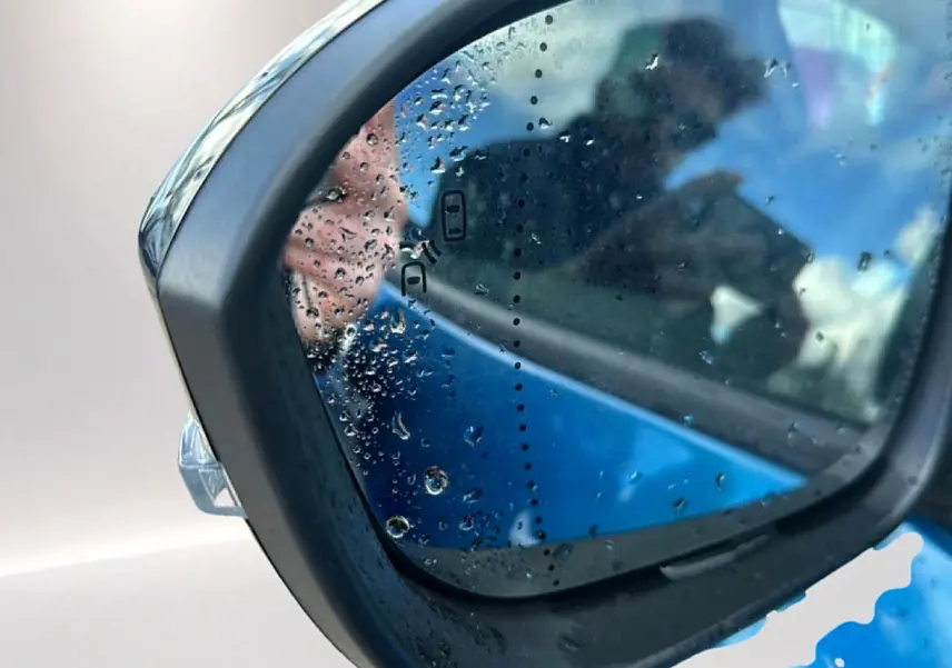 Rétroviseur extérieur gauche bleu outremer de Renault Austral 2026 avec gouttes d'eau et reflet flou.