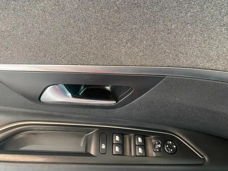 Gros plan sur la poignée intérieure et les commandes des vitres côté conducteur d'une Peugeot 3008 rouge de 2018.