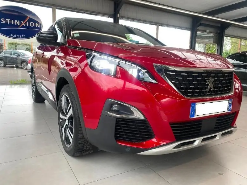 Peugeot 3008 rouge vue 3/4 avant droit en intérieur, avec calandre noire et feux LED allumés.