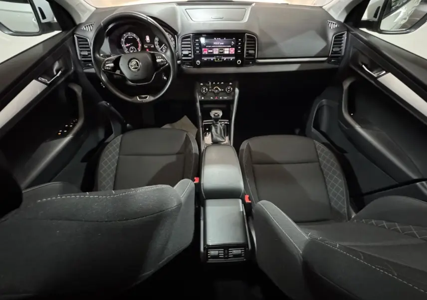 Vue intérieure avant du Skoda Karoq 1.5 TSI blanc, tableau de bord moderne avec écran tactile et volant multifonctions cuir.