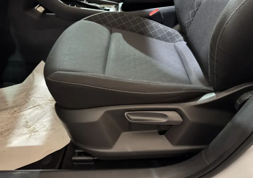 Gros plan sur le siège avant gauche gris foncé du Skoda Karoq blanc, montrant la manette de réglage latérale.