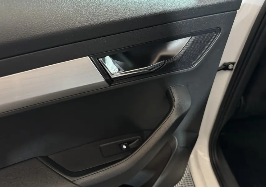Poignée intérieure côté gauche de la porte avant d'une Skoda Karoq blanche avec insert argenté et bouton de verrouillage.