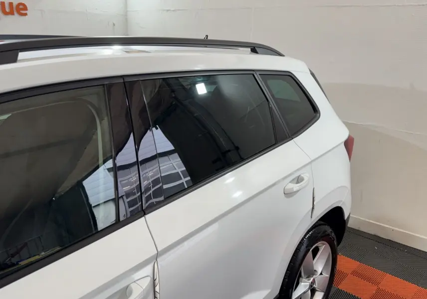 Vue côté droit arrière d'un Skoda Karoq blanc 2021 avec jantes alliage et barres de toit noires.