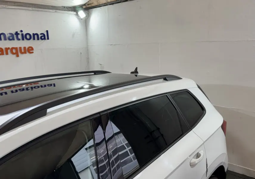 Vue côté droit arrière du SKODA KAROQ blanc avec toit panoramique et barres de toit noires visibles.