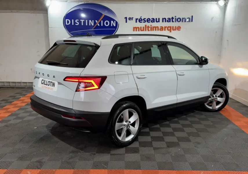 Vue 3/4 arrière droite d'un SUV SKODA KAROQ blanc avec feux arrière LED allumés dans un showroom.