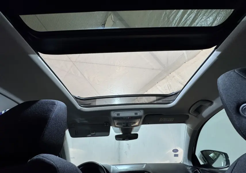 Vue intérieure avant du Skoda Karoq blanc 2021, mettant en valeur le toit panoramique et les sièges noirs.