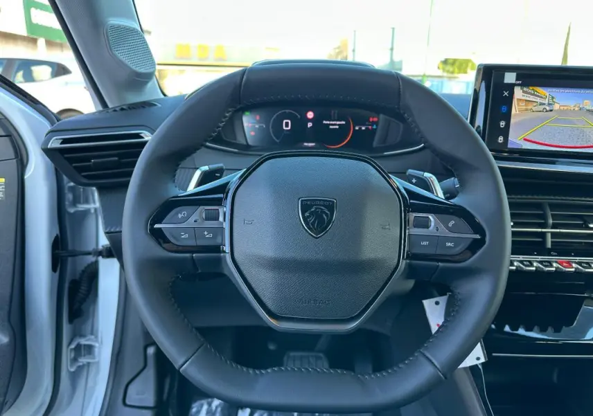 Vue intérieure centrée sur le volant cuir noir du Peugeot 208 blanc, avec cockpit numérique et écran tactile visible.