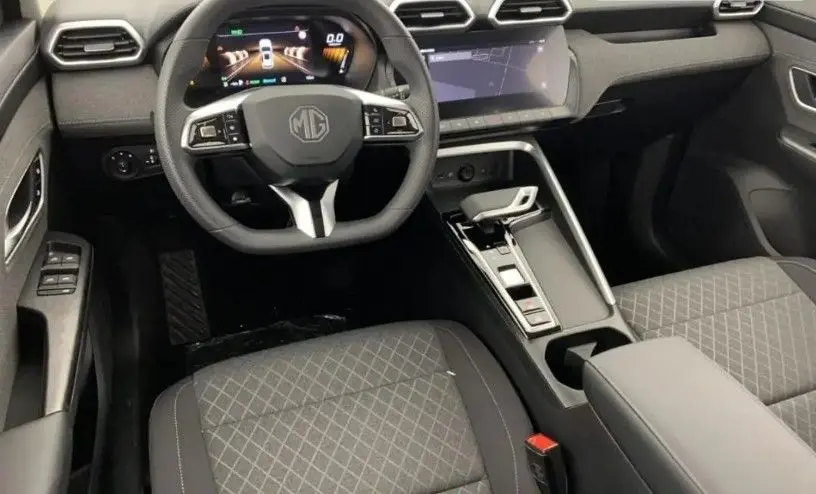 Vue intérieure avant du MG ZS 1.5 L Hybrid+ 2025, tableau de bord moderne avec écran tactile et sièges en tissu noir.