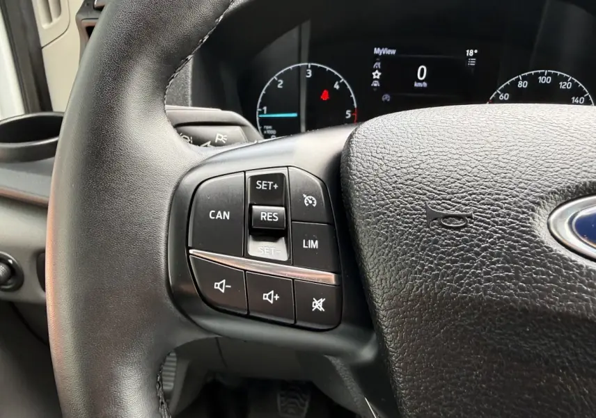 Gros plan sur le volant en cuir noir du Ford Transit Fourgon 2024 avec commandes intégrées et tableau de bord numérique.