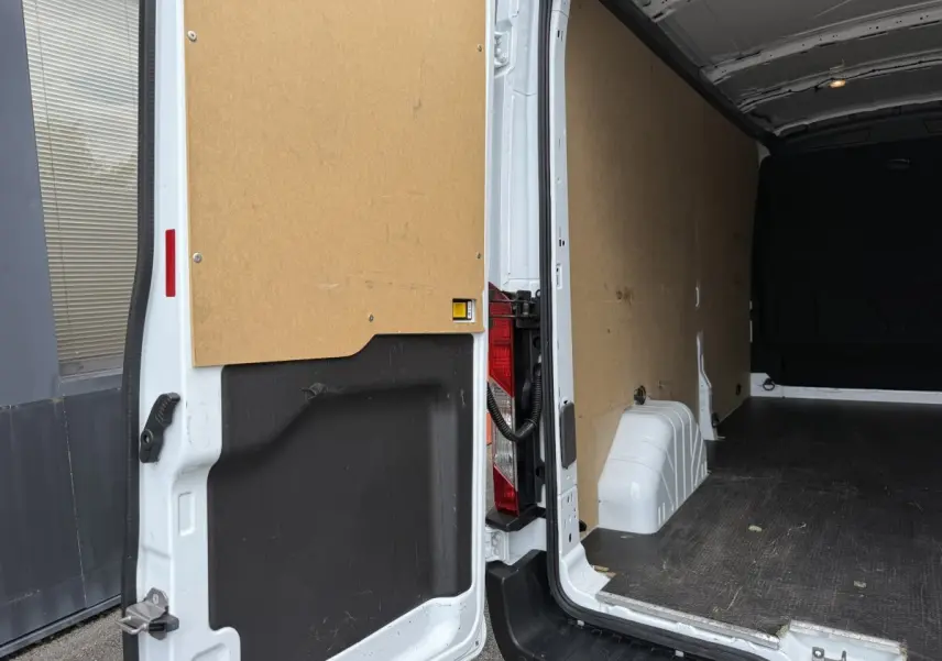 Vue arrière ouverte du fourgon Ford Transit blanc, montrant l'intérieur vide avec parois en bois et plancher noir antidérapant.