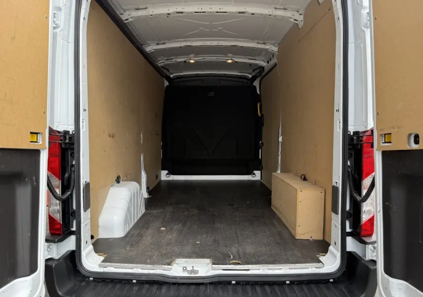 Vue arrière du fourgon Ford Transit blanc 2024 avec portes ouvertes, montrant l'espace de chargement vide et cloison pleine.