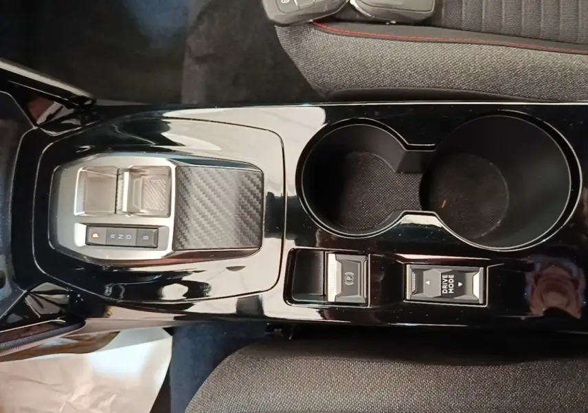 Vue plongeante sur la console centrale noire brillante du Peugeot E-2008 électrique avec sélecteur de vitesse et porte-gobelets.