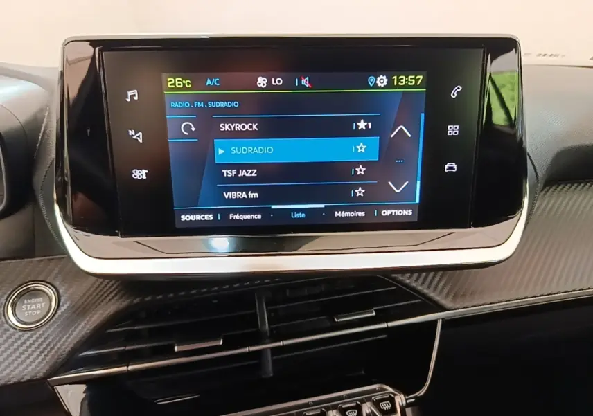 Écran tactile central allumé montrant les stations radio dans l’habitacle du Peugeot E-2008 électrique gris clair.
