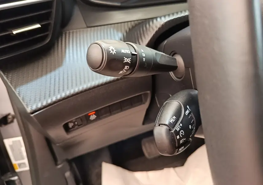 Gros plan sur les commandes au volant du Peugeot E-2008 électrique gris clair, avec réglages feux et régulateur de vitesse.