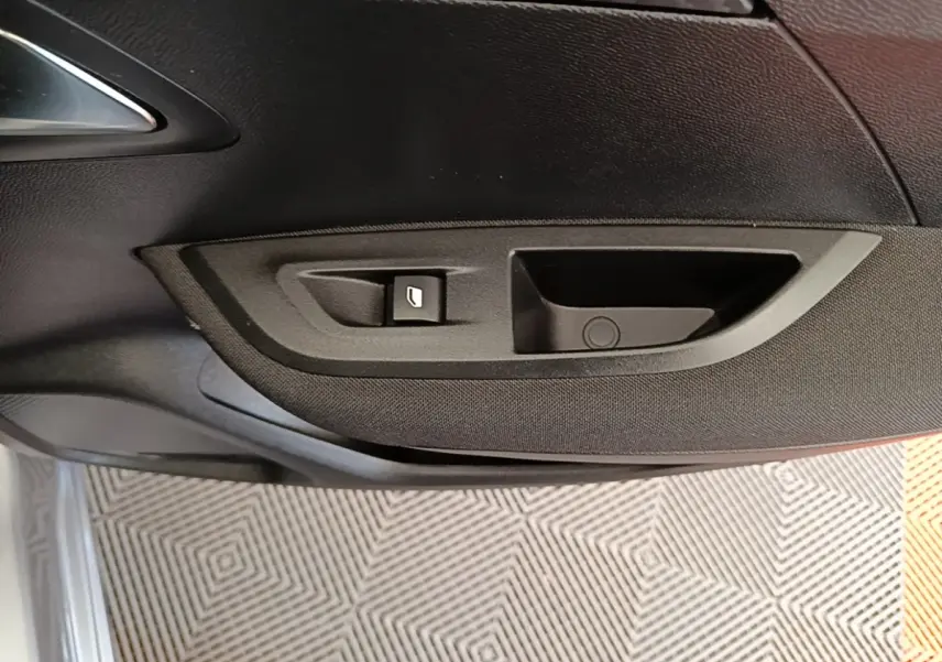 Gros plan sur la poignée intérieure et le bouton de lève-vitre côté conducteur du Peugeot E-2008 gris clair électrique.