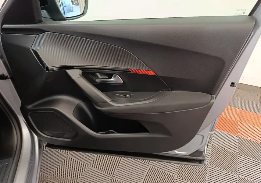 Vue latérale gauche de la porte intérieure gris clair du Peugeot E-2008 électrique avec insert carbone et bande rouge décorative.