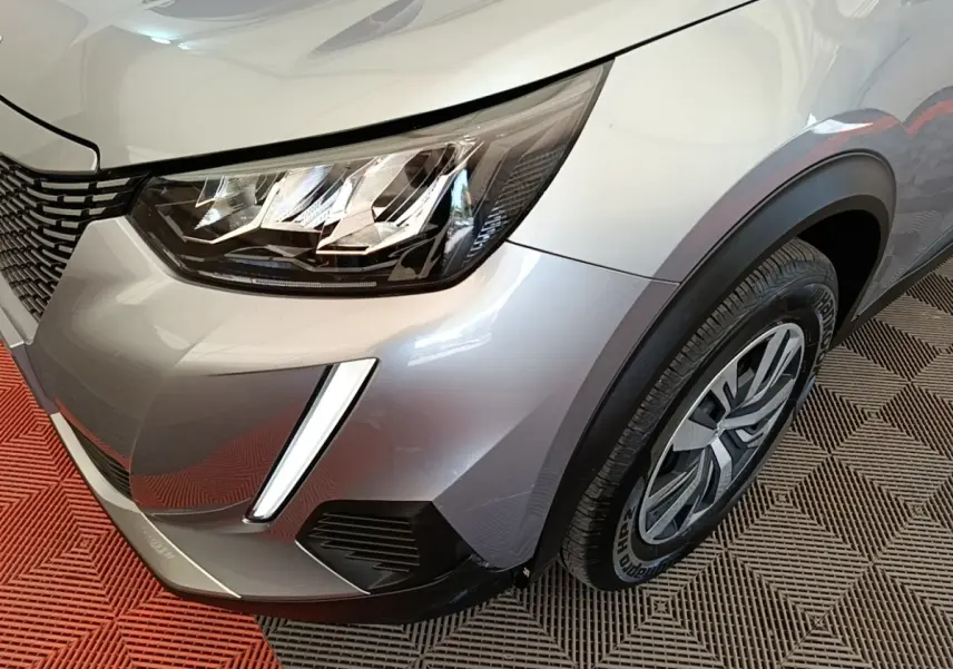 Gros plan sur l’avant droit gris clair du Peugeot E-2008 électrique avec phares LED et jante alu distinctive.
