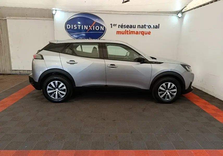 Profil droit d'un Peugeot E-2008 électrique gris clair 2023, avec toit noir et jantes distinctives en concession.