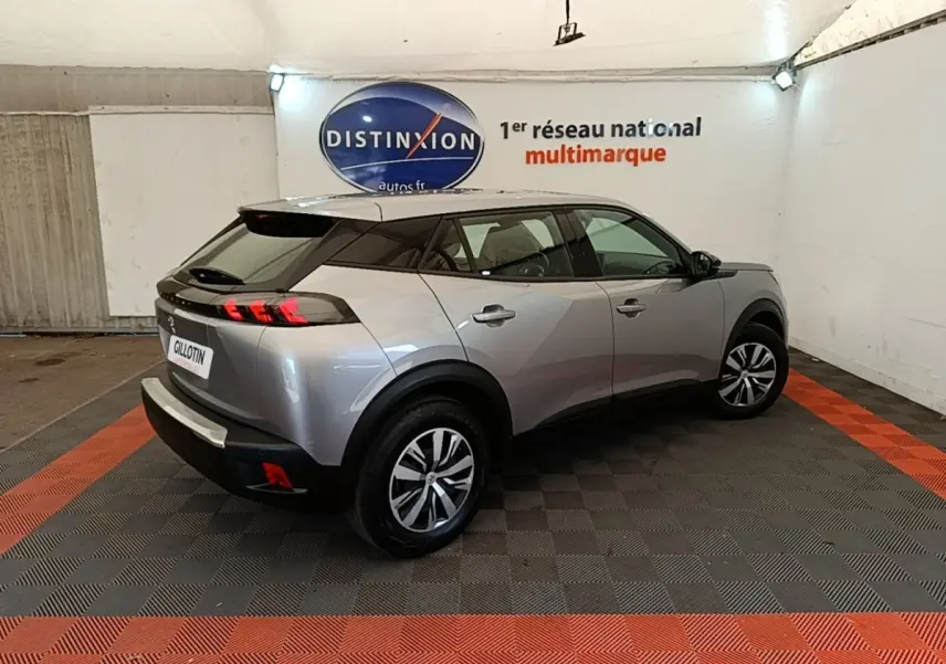 Vue 3/4 arrière droite d’un Peugeot E-2008 électrique gris clair avec toit noir dans un showroom.