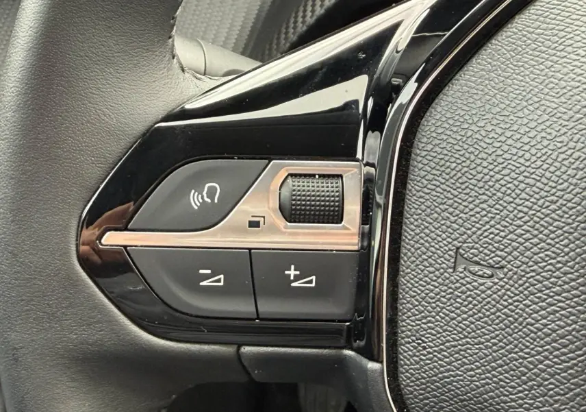 Gros plan sur les commandes audio et vocales noires sur le côté gauche du volant de la Peugeot 208 noir Perla Nera.