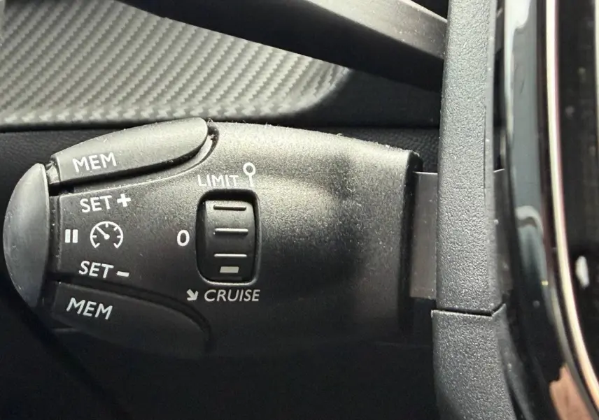 Gros plan sur la commande de régulateur de vitesse noire dans l’habitacle du Peugeot 208 noir Perla Nera.