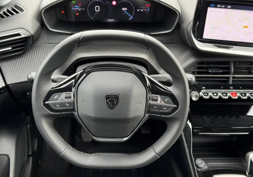 Vue rapprochée du volant compact noir de la Peugeot 208 2025 avec tableau de bord numérique et écran tactile latéral.