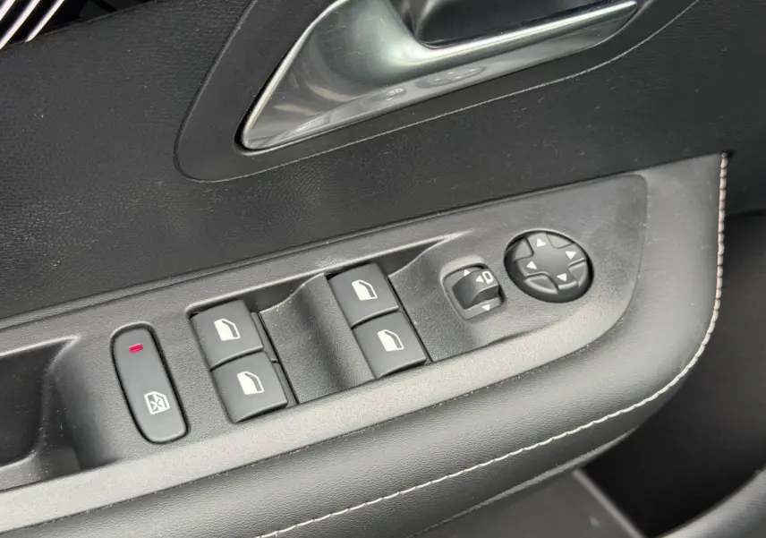 Gros plan sur la commande des vitres et rétroviseurs côté conducteur de la Peugeot 208 noir Perla Nera avec surpiqûres blanches.