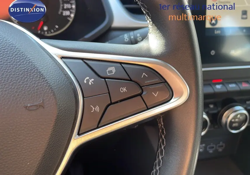 Gros plan sur les commandes au volant en cuir noir du Renault Captur gris Cassiopée, avec tableau de bord et écran tactile en arrière-plan.