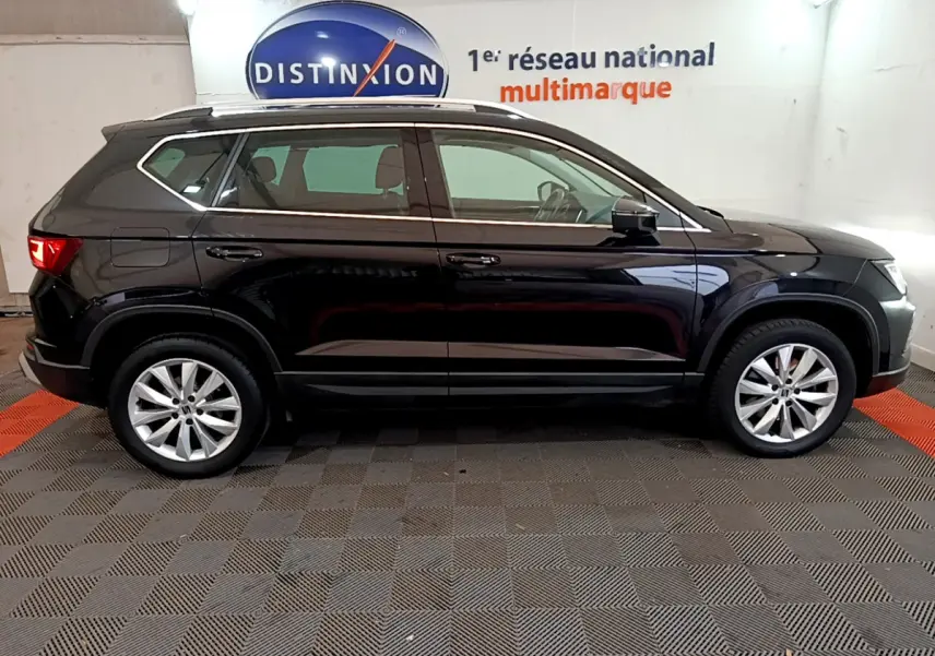 Profil côté gauche d'un SUV SEAT Ateca noir 2022 avec jantes alliage et barres de toit chromées dans un showroom.