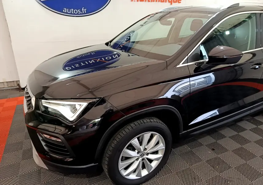 Vue 3/4 avant droit d'un SEAT Ateca noir brillant avec jantes alliage et phares LED allumés en intérieur showroom.